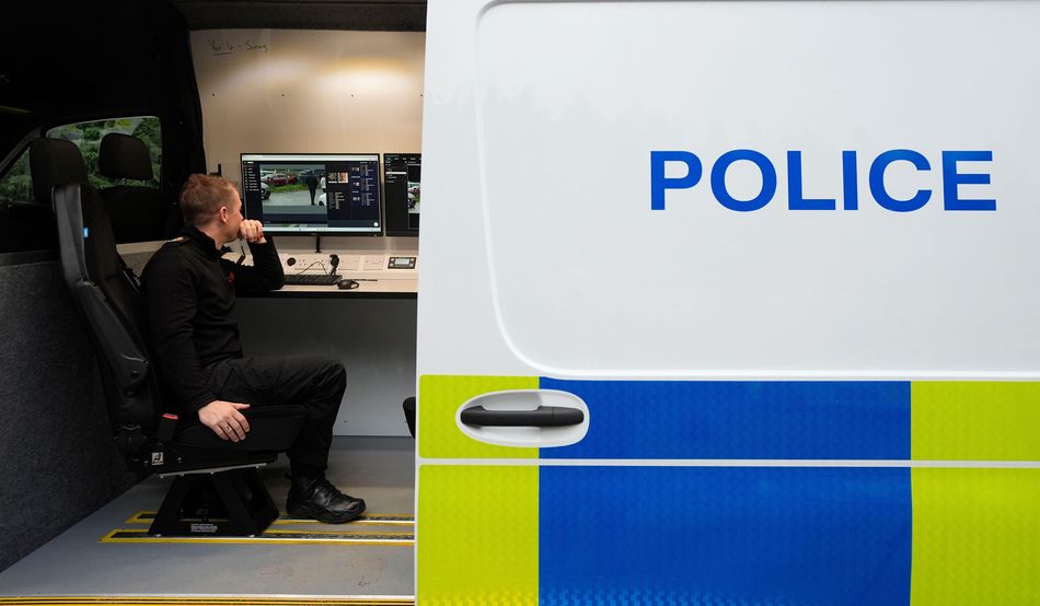A police officer monitors a screen showing surveillance film. He sits on a black chair inside a police van. Image: Alamy