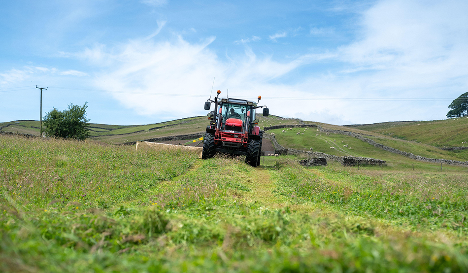 Farmer mowing a wildflower meadow for winter livestock feed in the Yorkshire Dales, UK.
