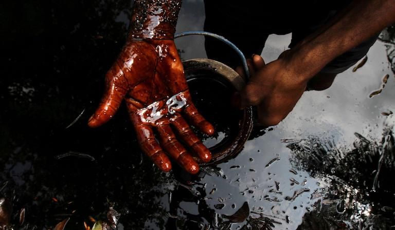 A man samples crude oil at the bank of a polluted river in Nigeria's delta region.
