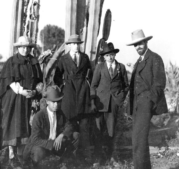 Frieda Lawrence, Willard Johnson, a Mexican, D.H. Lawrence (from left to right) standing in front of a cactus, with a second Mexican crouching in front of the standing group.  The photograph was taken by Witter Bynner at Orizaba, Mexico in 1923.