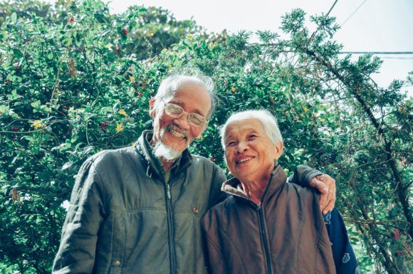 A middle-aged couple smile together in front of a tree.