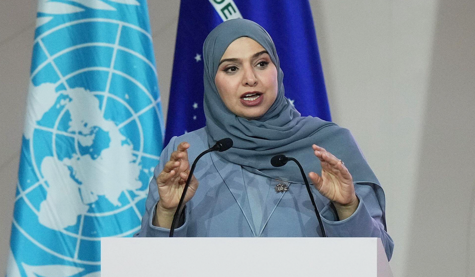 Amna Al Shamsi, minister of climate change and environment of the United Arab Emirates, speaks during a plenary session at the COP30 in Belém, Brazil. Al Shamshi is speaking at a white podium with the blue UN flag behind her. She is also wearing a blue jacket and blue headscarf. Image: Associated Press