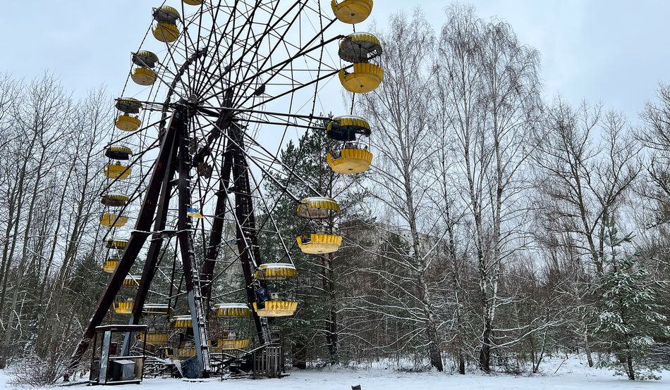 In snowy Pripyat, an abandoned ferris wheel with yellow booths stands still