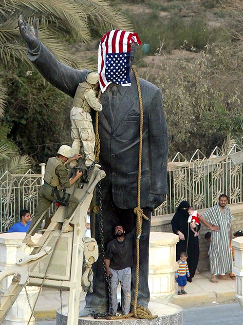 US Marines cover the statue of Iraqi President Saddam Hussein with the US flag in Baghdad's al-Fardous street 09 April 2003 as they prepare to bring it down. They removed it shortly afterwards and replaced it with an old Iraqi flag.     AFP PHOTO/Patrick 