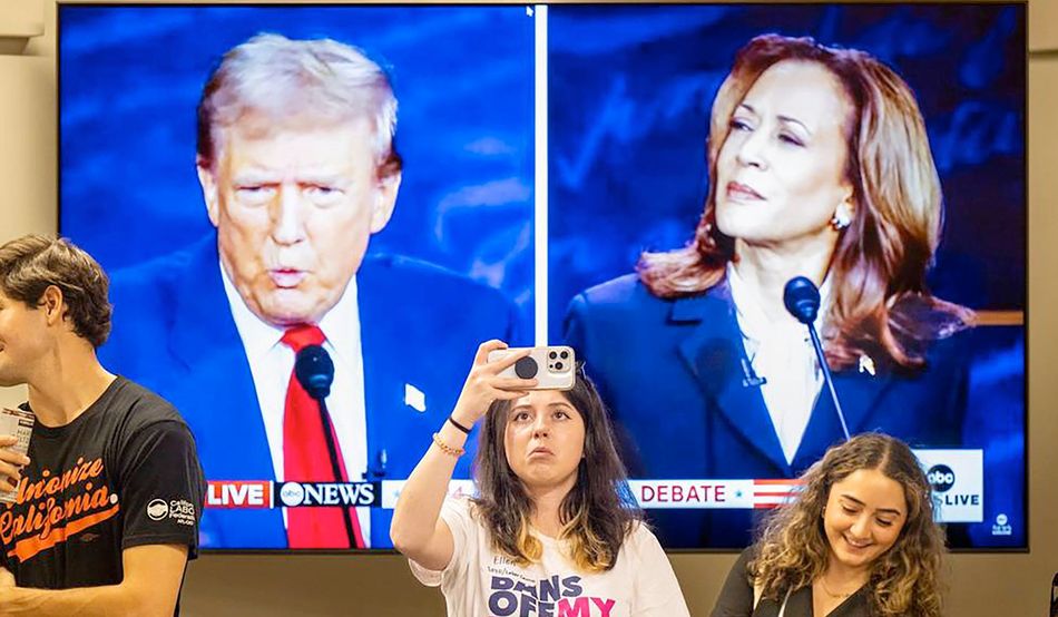 A young woman takes a photograph on her mobile phone. Behind her is a TV screen of the debate, split between Trump and Harris. Uncomfortable viewing: a young woman photographs the audience at a presidential debate watch party in Sacramento, California. Photo: © Chronicle / Alamy Stock Photo